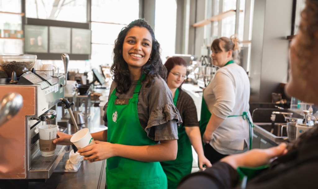 A smiling Starbucks barista pours a hand-crafted coffee.