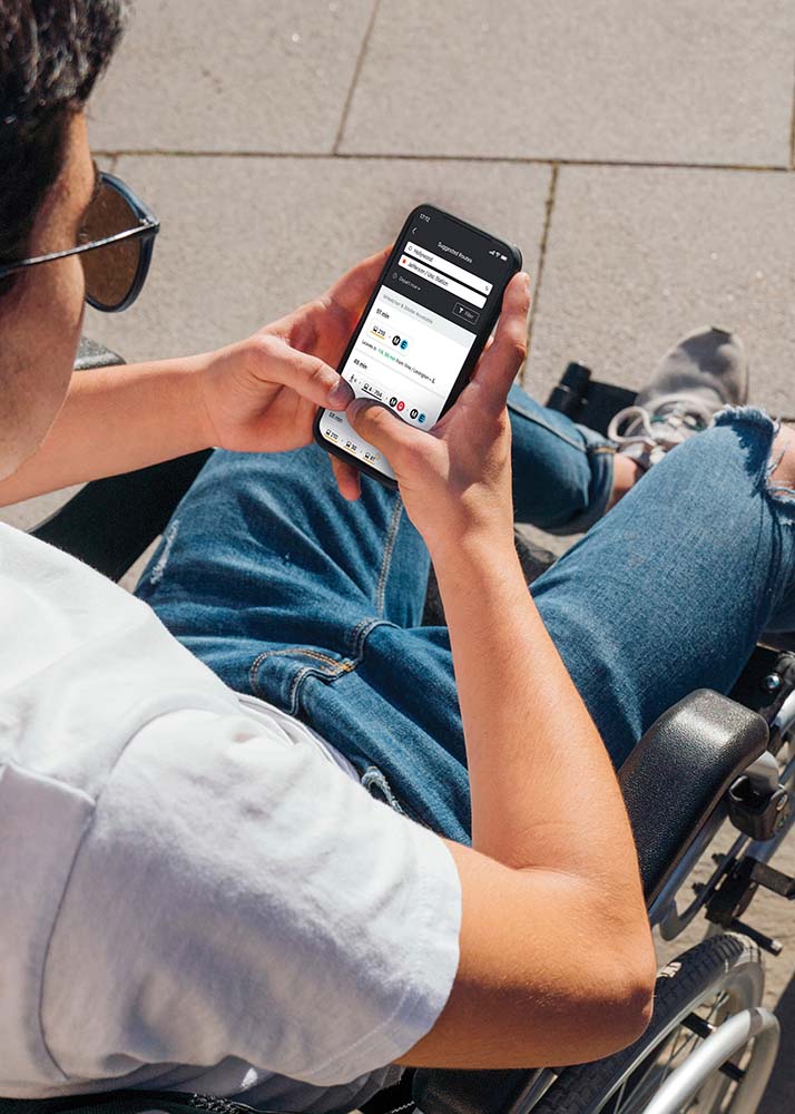 Man in wheelchair on a street uses Moovit app on his phone