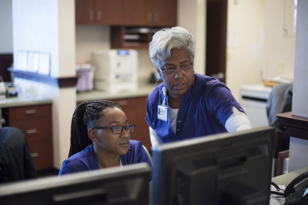 Two Novant Health employees consult monitors at a nursing station.
