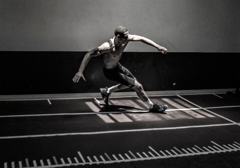 An athlete is shown moving sideways on an indoor track.