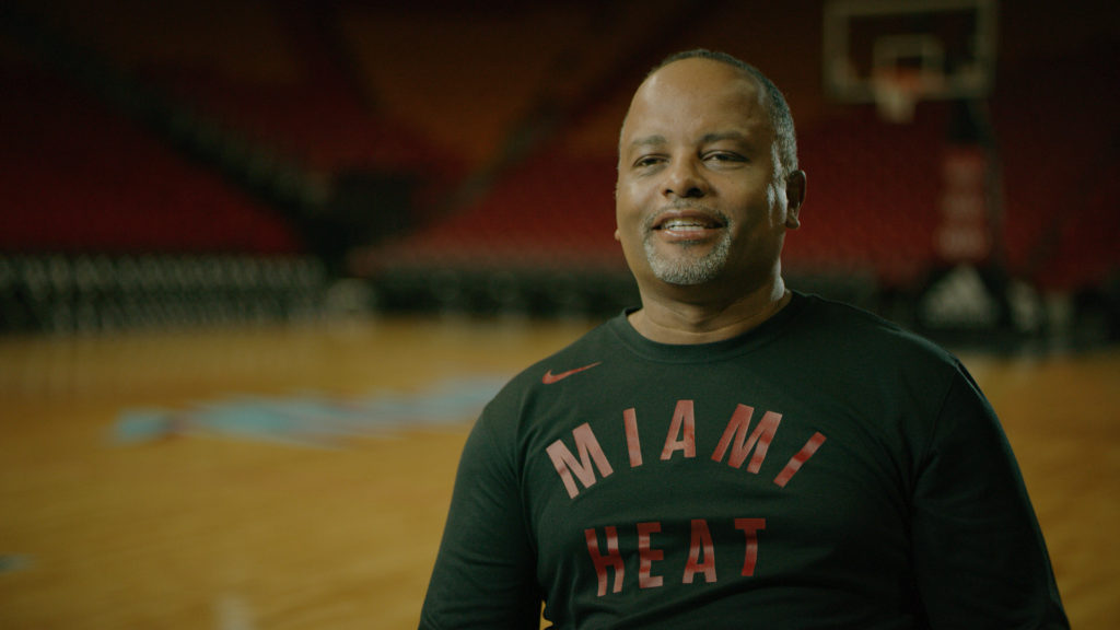 Miami Heat executive Edson Crevecoeur sits in an empty AmericanAIrlines Arena, smiling. 