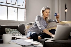 woman on couch holding credit card and looking at computer screen
