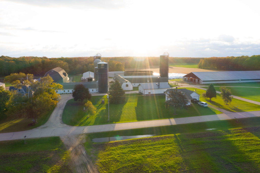 A Wisconsin farm, affiliated with Land O'Lakes, shown from above as the sun casts shadows on the green fields and silos.