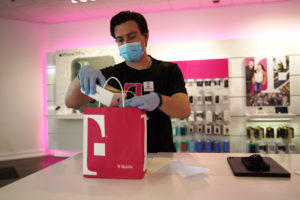 A T-Mobile employee in gloves and a mask bags a purchase