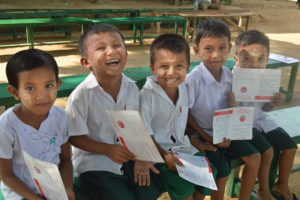 Photo of a group of boys in Myanmar, smiling and showing their vaccination certificates.