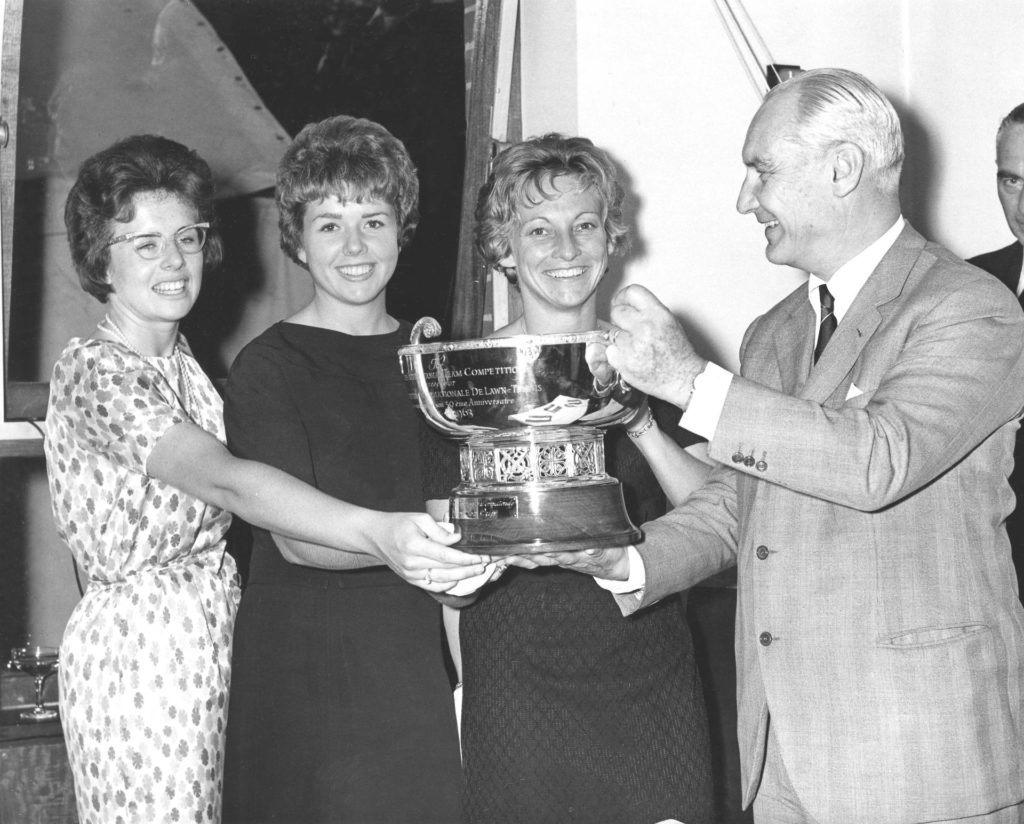 A black-and-white photo shows three women's tennis champions smiling as they accept a trophy for winning the 1963 Fed Cup