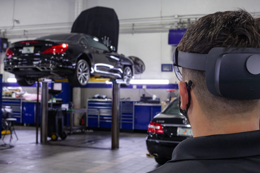 An auto technician wearing a HoloLens 2 look at a service bay where a car is up on a lift. 