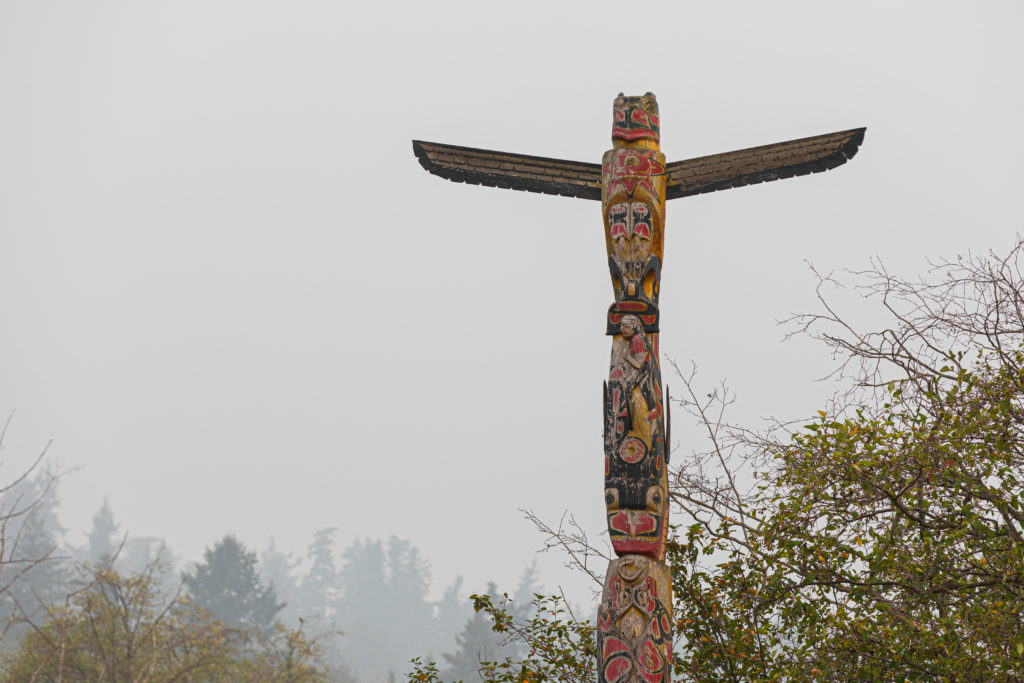 A Samish totem pole stands outside against a smoky sky. 
