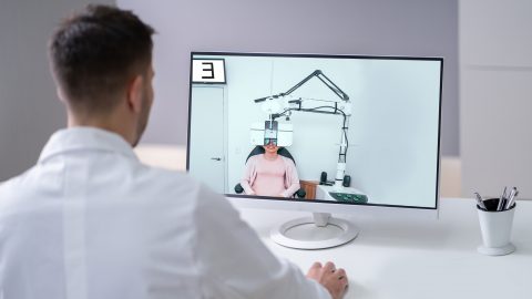 An eye doctor chats via a computer screen with a patient undergoing a refraction exam.