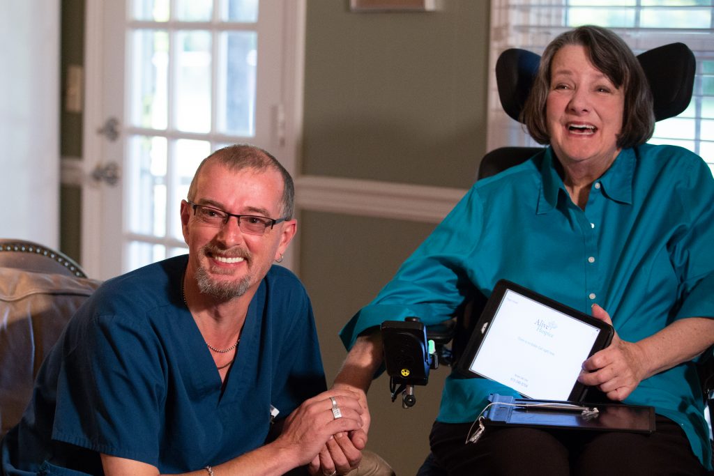 Photo of a male caregiver holding the hand of a woman in a wheelchair, both of them smiling