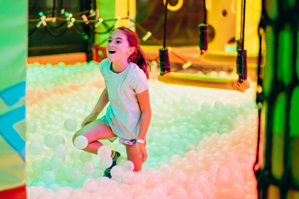 A girl lands feet first and smiling into a large vat of plastic balls.