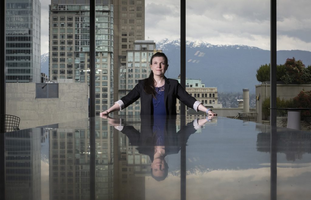 Katie Peters, staff developer for TELUS, sitting at a conference desk in the company’s headquarters, sky and mountains reflected in the desk’s glossy surface.