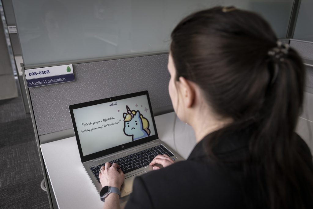 Photo of Katie Peters working on a computer at TELUS headquarters and showing a slide with a unicorn on one of its display boards.