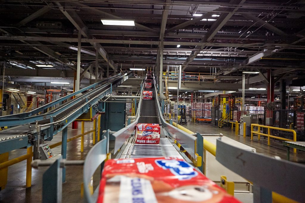 Plastic-wrapped packs of Charmin toilet paper move along on a conveyor belt at a P&G manufacturing facility.