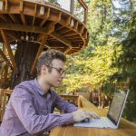 Employee working on a Surface device at an outside deck on a wooden platform built into in a tree