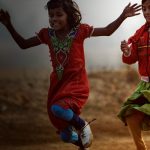 Two young girls playing soccer in a dirt field in rural India