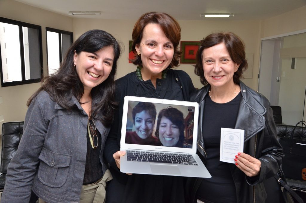 Three women holding a laptop that displays two more women