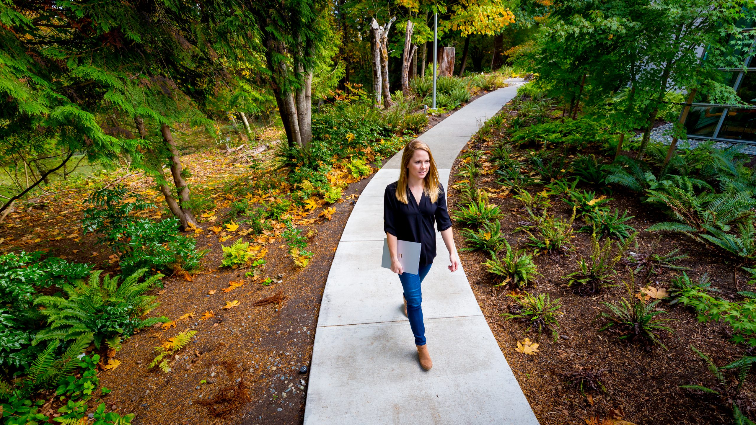 woman walking on concrete path through nature area