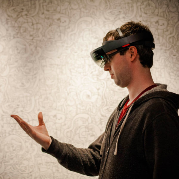 A photo of a Microsoft employee doing a "bloom" gesture with his hand while wearing a HoloLens