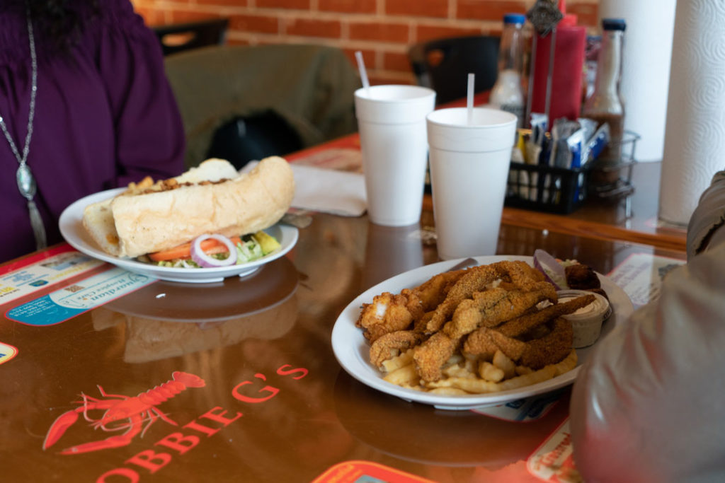 A photo of a plate of fried catfish and plate with a po-boy sandwich on a table in a restaurant