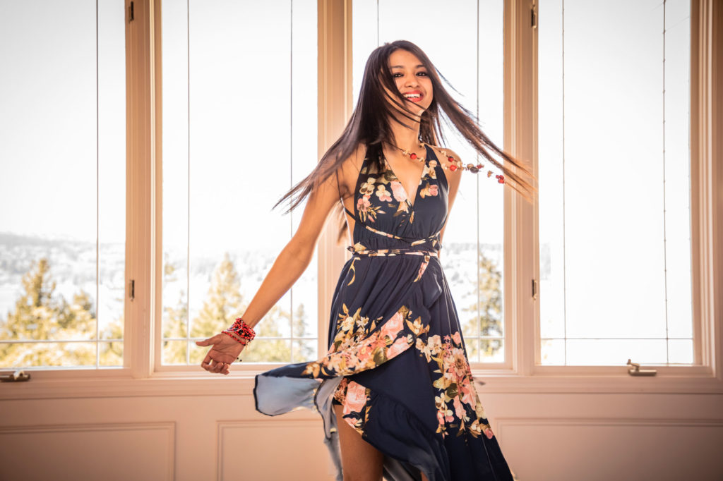 A woman in a black dress twirls in front of a window