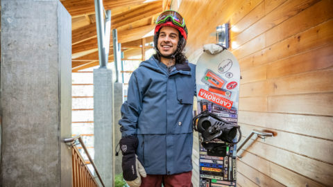 A man stands holding a snowboard while wearing snowboarding gear