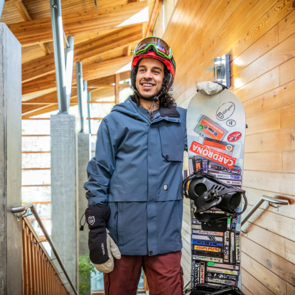 A man stands holding a snowboard while wearing snowboarding gear
