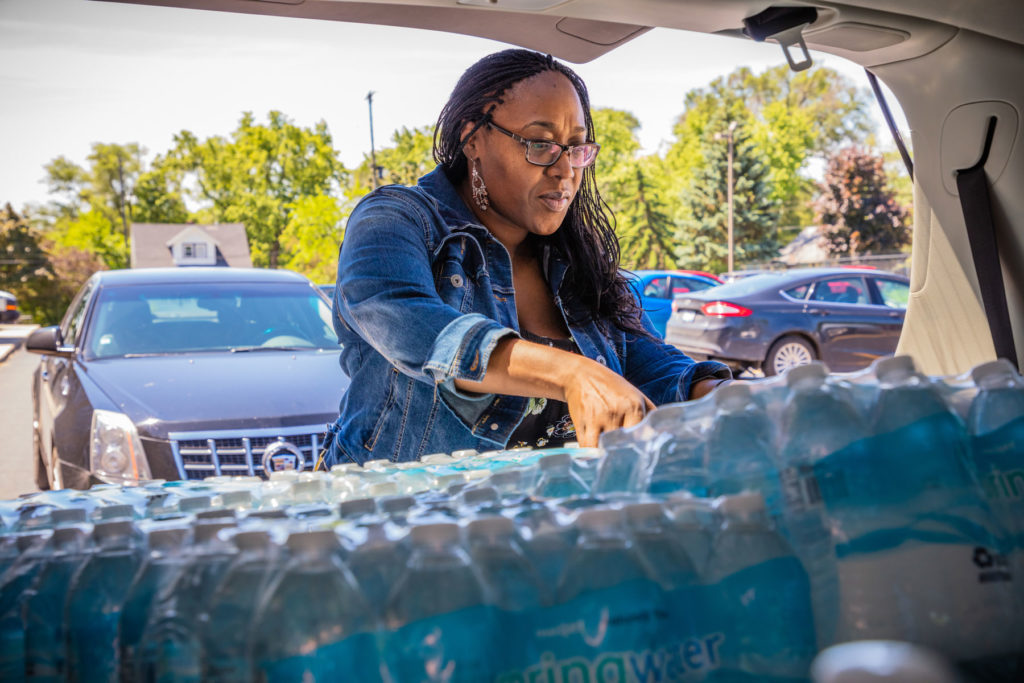 Woman reaches into the trunk of her car for a big pack of water bottles