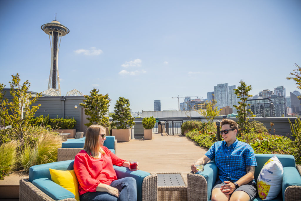 Two women sit on a sunny deck with the Space Needle in the background