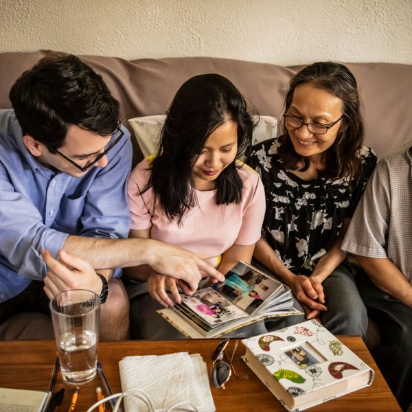 Huong Haley sitting on a couch with her husband and her parents, looking at scrapbook photos together