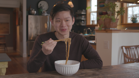 A man eats beef noodle soup using chop sticks