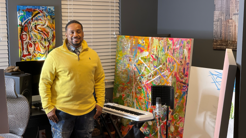A photo of a man standing next to an art painting and a piano keyboard