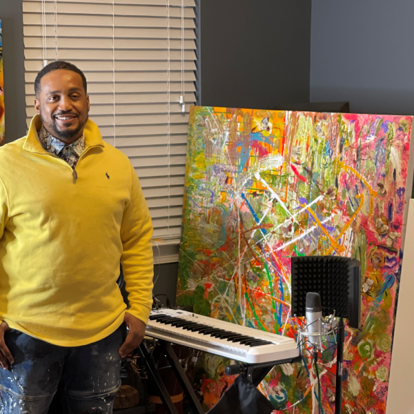 A photo of a man standing next to an art painting and a piano keyboard