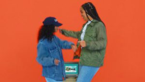 Two women moving next to each other in Hardwear clothing, in front of a red background.