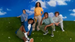 A group of models wearing Hardwear clothing, sitting and standing on grass and in front of a blue background.
