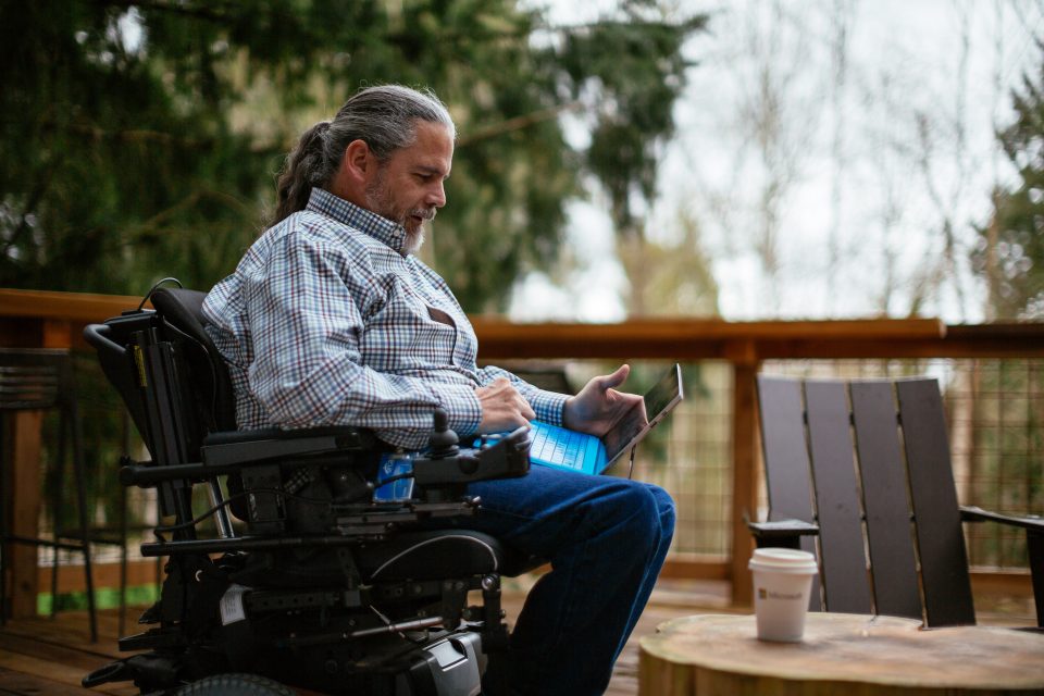Stuart Pixley, a man who uses a wheelchair, holds a laptop on his lap while outside. Accessibility, disability, and inclusion collection.