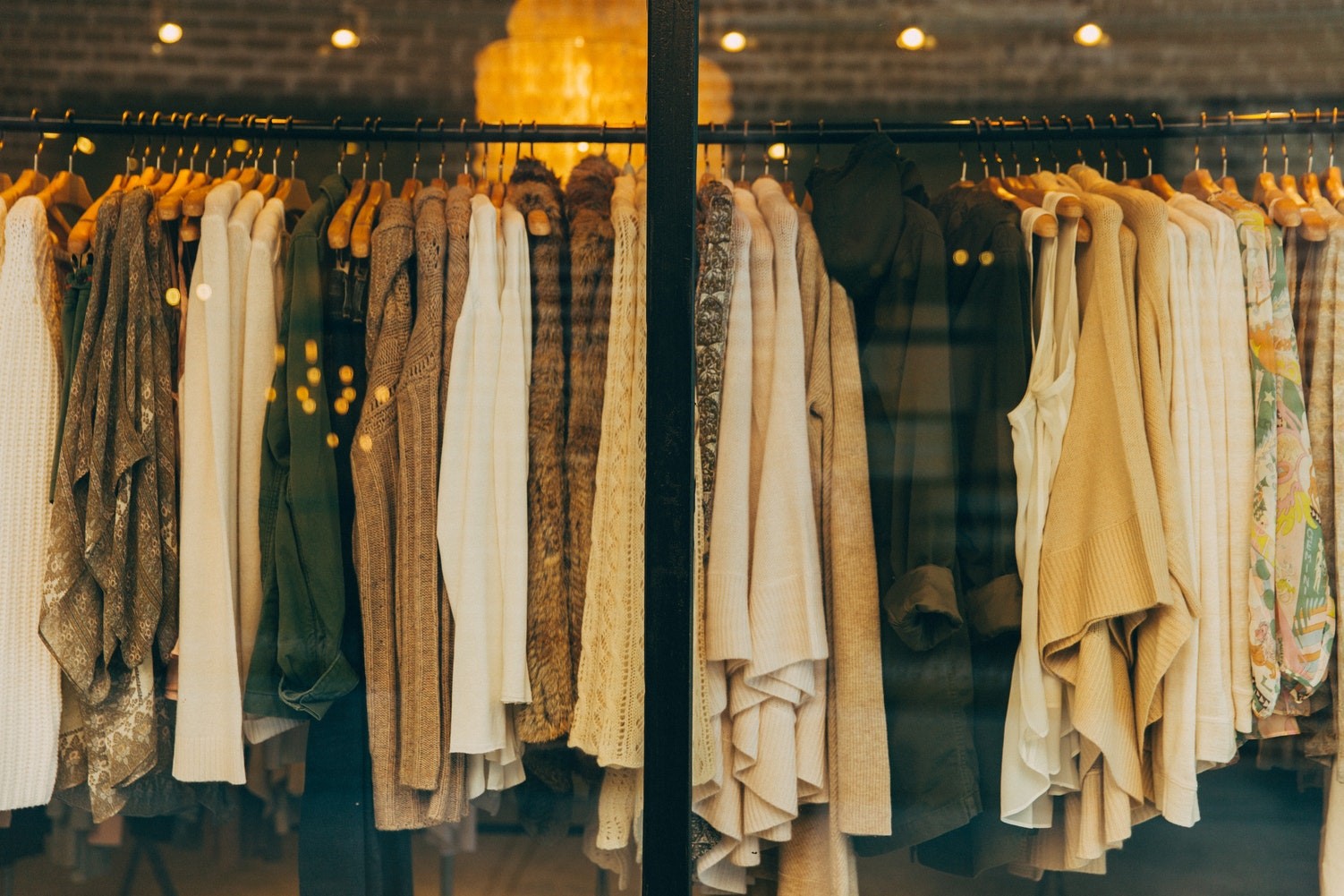 Das Bild zeigt eine Kleiderstange, auf der verschiedene Kleidungsstücke aufgereiht hängen. Die Farbgebung ist sehr natürlich, erdige Farben wie braun, creme und grün dominieren.