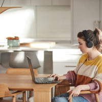 Eine Frau mit Kopfhörern sitzt an einem Tisch und arbeitet an einem Laptop.
