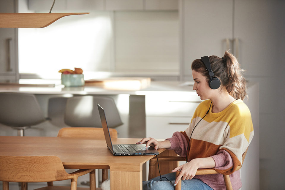 Eine Frau mit Kopfhörern sitzt an einem Tisch und arbeitet an einem Laptop.