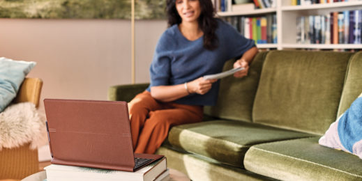 Eine Frau sitzt zu Hause auf ihrem Sofa und führt eine Telefonbesprechung mit ihrem Laptop durch.