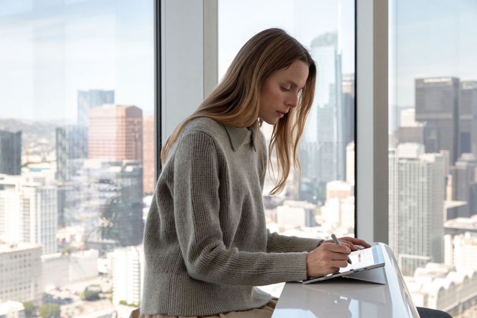Junge Frau sitzt an einem Tresen und bedient ein Surface Pro mit einem digitalen Pen