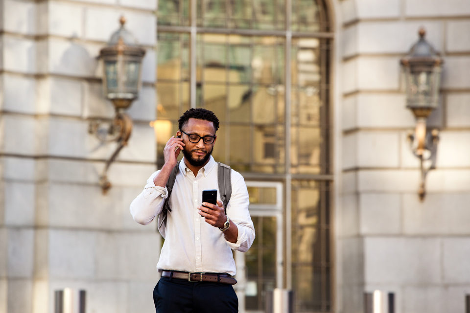 Ein Mann steht vor einem Gebäude und schaut auf sein Handy.