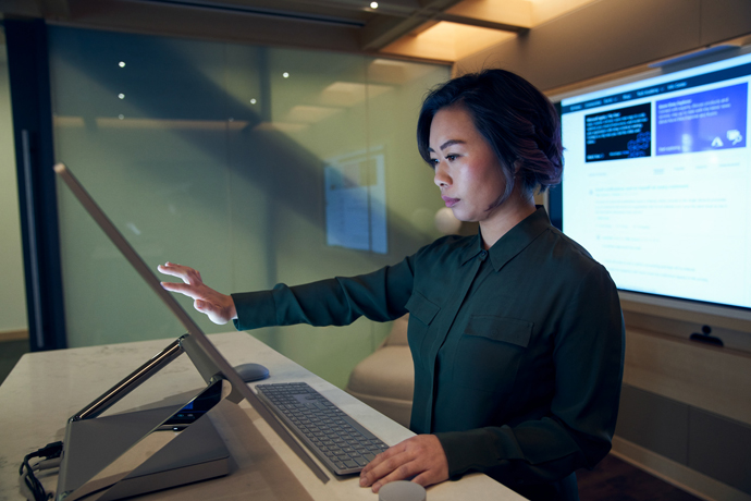 Seitenprofil einer Frau, die in einem dunklen Hemd in einem Büro an einem Microsoft Surface Studio arbeitet.