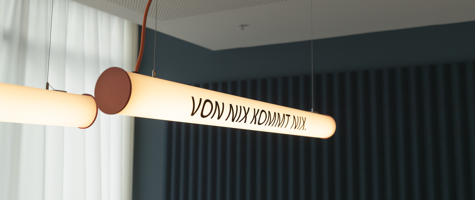 Zwei Deckenlampen im Regional Office Hamburg, auf denen "Von nichts, kommt nichts" steht.