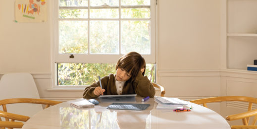 Datenschutz und Datensicherheit in Bildungseinrichtung. Kind das an einem Tisch zu Hause an einem Surfacegerät Schularbeiten erledigt.