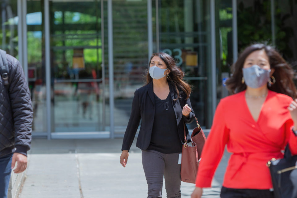 Drei Menschen verlassen ein Bürogebäude, sie tragen Masken.