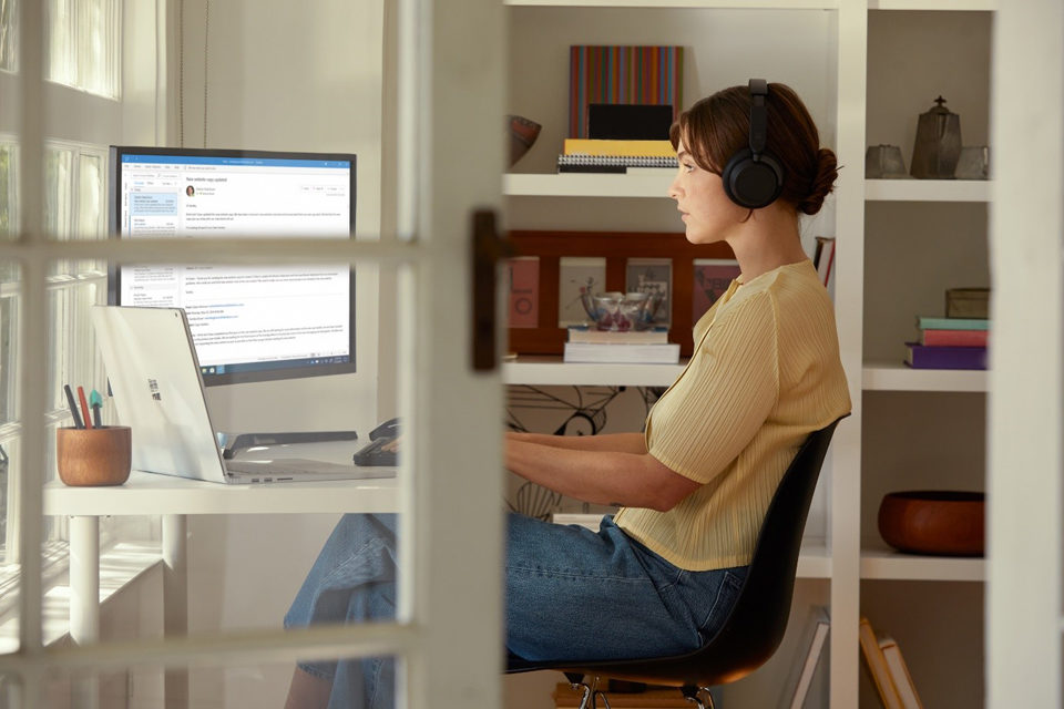 Aus seitlicher Perspektive sieht man eine Frau an ihrem Surface Studio im Home Office arbeiten