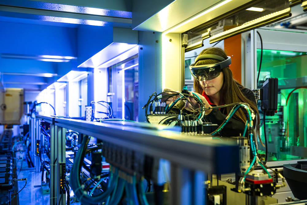 Eine Frau arbeitet mit der HoloLens in der Verbindungstechnik. Um sie herum sieht man Kabel und Leitungen.