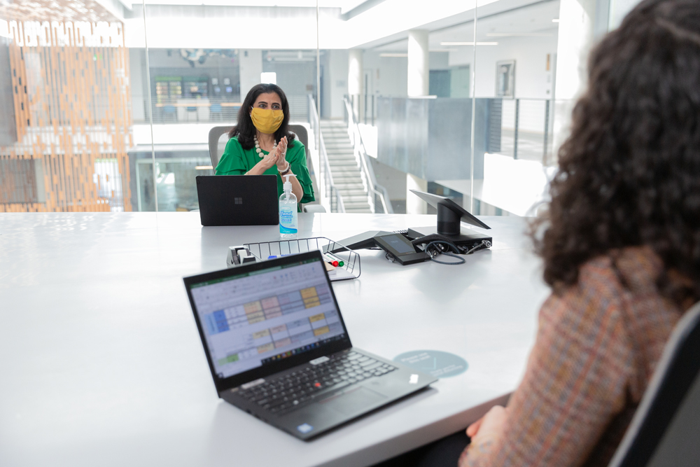 Zwei Frauen sitzen in einem Büroraum mit ihren Laptops, sie tragen Masken.