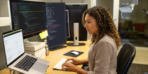 Eine Entwicklerin, die am Büroarbeitsplatz eines Unternehmens arbeitet. Sie hat ihren Arbeitsbereich mit einem Multi-Monitor-Setup angepasst.